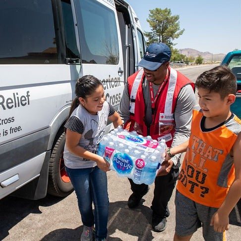 Red Cross volunteer carrying a case of water for children.