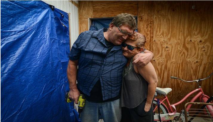 Jacques and Susan hugging in front of their home.