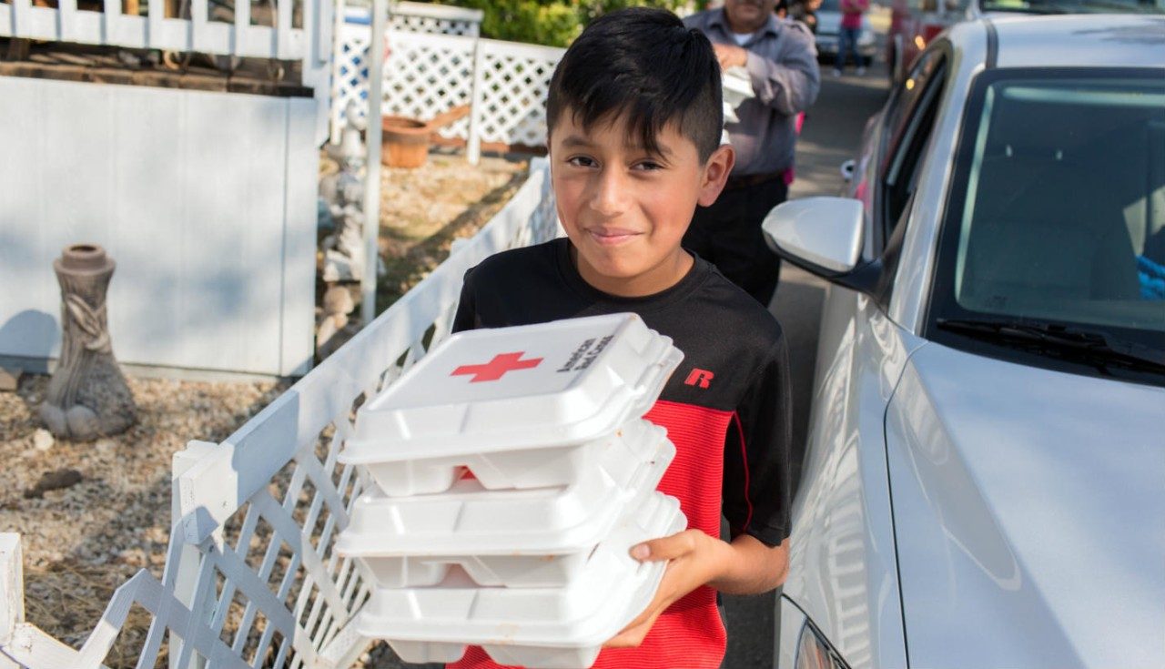 A boy carrying boxes of meals received from a Red Cross volunteer.