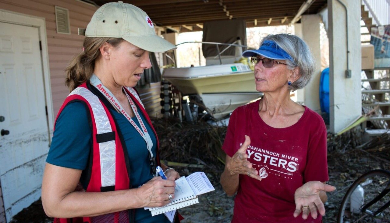 A Red Cross volunteer talking to a woman while writing information on a notepad.