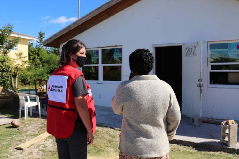 Firstina Swain standing next to a Red Cross volunteer outside of her home.