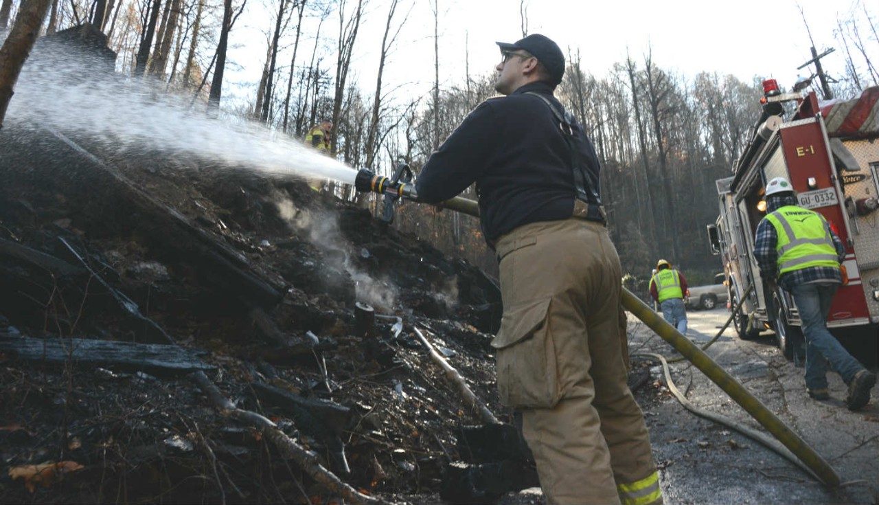 An emergency responder spraying water from a hose to put out a fire.