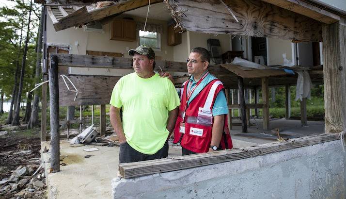 David standing outside of his damaged home with a Red Cross volunteer.