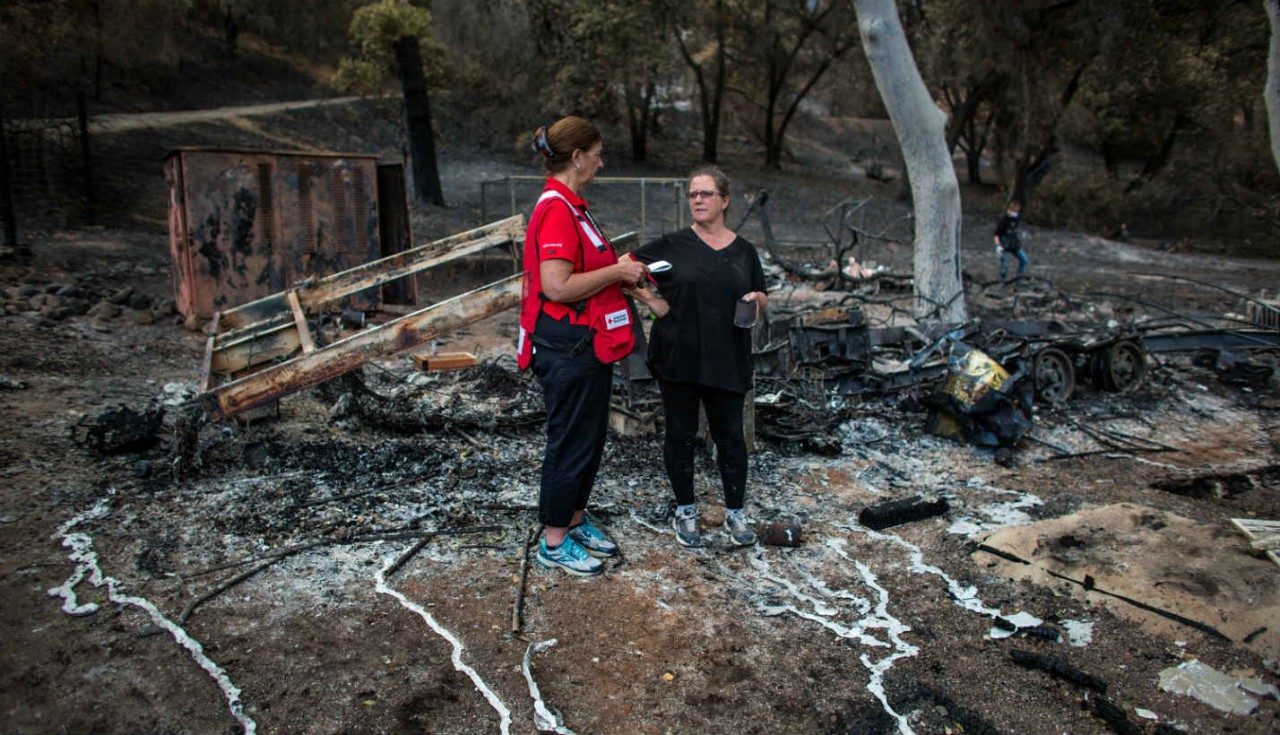 A Red Cross volunteer meeting with a woman at a disaster site.