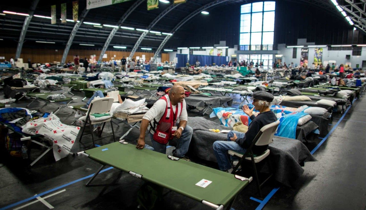 A Red Cross volunteering chatting with a man at a shelter.