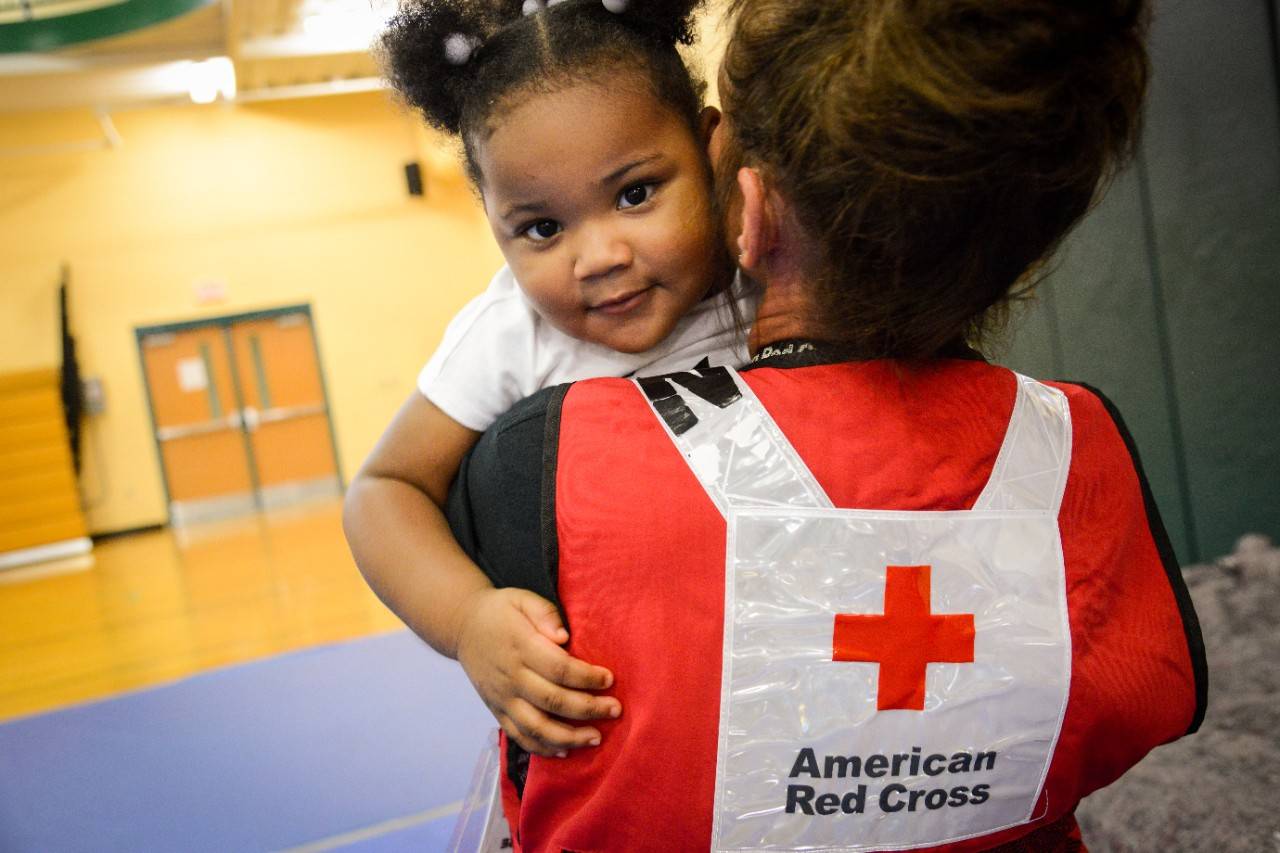 September 5, 2019. Jacksonville, Florida.American Red Cross nurse Jana Cearlock coaxes hugs and smiles from 2-year old Karmin Nelson, a resident, along with her great-grandmother at the Legends Center evacuation shelter in Jacksonville, Florida. Karmin’s great-grandmother, Minnie McDonald came with Karmin to the shelter to be in a safe place as Hurricane Dorian passed near the Jacksonville area. It was the third time in three years that Minnie had come to this same shelter. “When the say E, I evacuate,” said Minne.Photo by Daniel Cima/American Red Cross