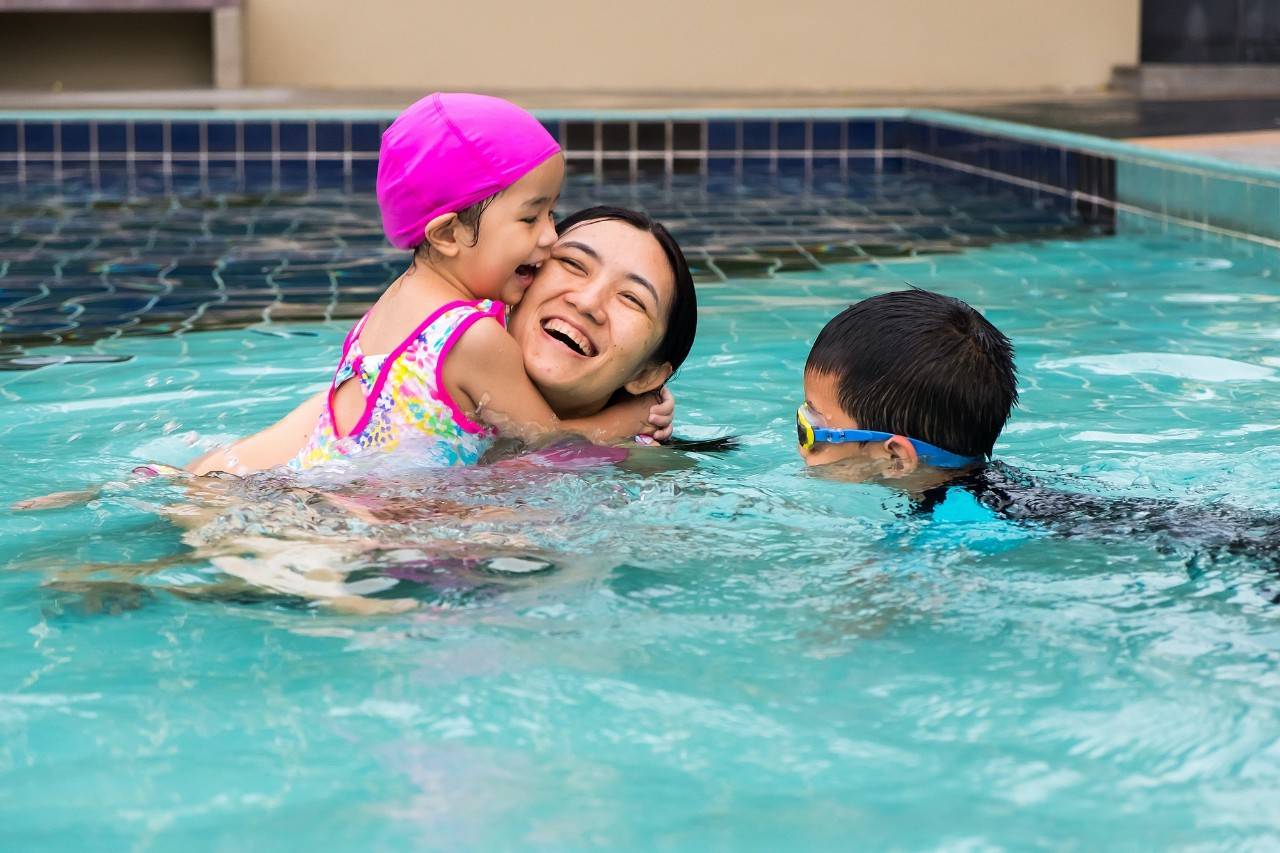 family spent time to swim in swimming pool. they enjoy playing together with laughing.