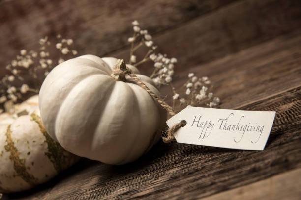 This is a close up photo of a group of small white pumpkins with a card on a wood table background. There is space for copy. This is a nice high key image that would work well for autumn, Thanksgiving and a holiday Halloween season in the fall.