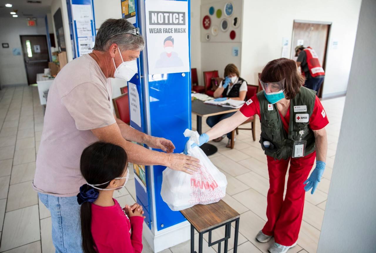 April 26, 2020. Livingston, Texas.
Cheryl Thomas, a nurse for the American Red Cross, hands a meal to Marc Sasso and his daughter Rachel, 6 yrs old, as part of Covid-19 screening protocol at a hotel in Livingston, TX on Sunday, April 26, 2020 where the Red Cross is providing emergency lodging for people whose homes were damaged or destroyed by the powerful tornado that hit Onalaska, TX on April 22. The Red Cross is using a hotel to shelter people, rather than opening traditional style congregate shelters due to the Covid-19 pandemic.
Photo by Scott Dalton/American Red Cross