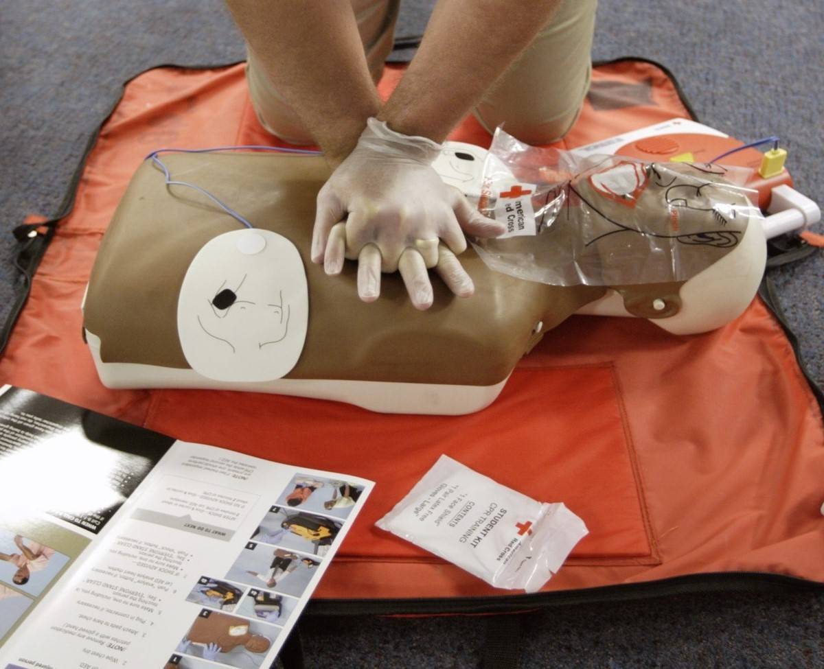 gloved hands performing CPR on a training device