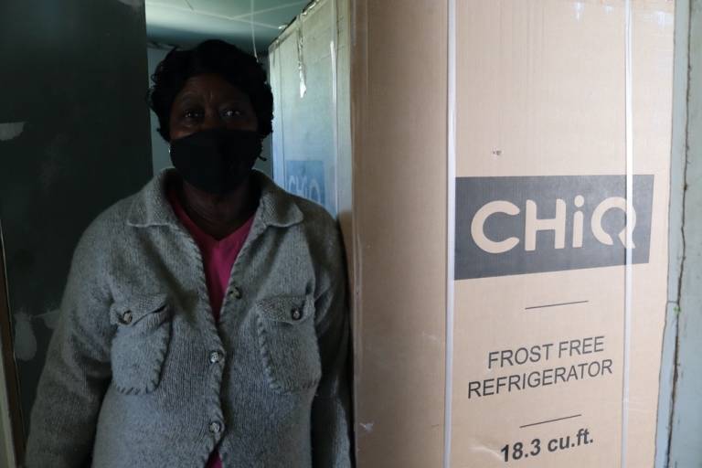 woman stands with a refridgerator in packaging