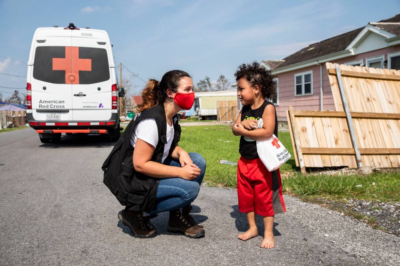 September 3, 2021. Larose, Louisiana. Stefanie Arcangelo of the American Red Cross shares a comfort kit and a smile with a child after Hurricane Ida left him, his three siblings and his mother, Yvonne Padilla Lucca without power and with damage to their home, in Larose, Louisiana on September 3, 2021. In some of the hardest hit parishes, like Larose, the Red Cross has emergency response vehicles circulating through accessible areas to distribute critical supplies including water, comfort kits and ready to eat meals. Photo by Scott Dalton/American Red Cross
