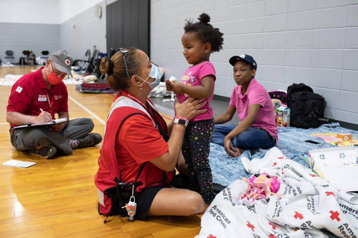 September 27, 2022. Clearwater, FloridaRed Cross volunteer Martha Narvaez entertains Serenity, age two, at the Red Cross Evacuation Shelter in Clearwater, Fl. Anxiety was growing for Imani Miley, Serenity's mom, as Hurricane Ian approached their home in nearby St Petersburg. She survived Hurricane Irma just a few years ago, but that was before she had the added responsibility of a young daughter. She was relieved when her friend called and told her about the evacuation shelter at the Ross Norton Community Center. "They're really nice here," said Miley pointing towards Martha Narvaez with a smile. "I can appreciate this." Narvaez later revealed that she was the one who found the new doll for Serenity. "I was in logistics in the Army for 27 years," Narvaez said, "and I know about "getting stuff" for people. They are so grateful and I'm just glad that we can help. It's why I love being a Red Cross volunteer."Photo by Marko Kokic/American Red Cross