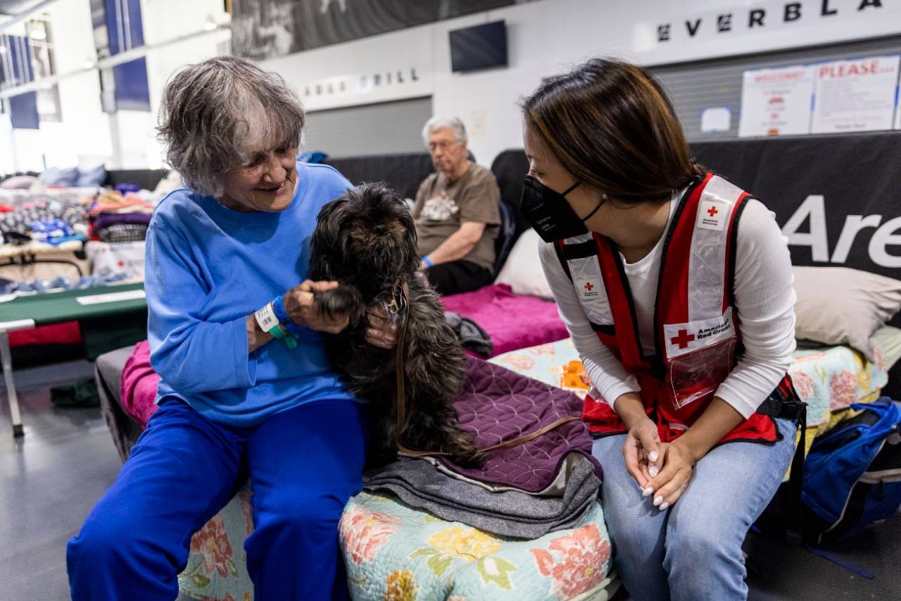 October 9, 2022. Estero, Florida.
Red Cross volunteer Jenn Thai checks in with Ginny Thornhill and Jack Sahrok, who each brought their dog with them to a pet-friendly Red Cross shelter at the Hertz Arena in Estero, FL. Red Cross shelter workers are doing all they can to welcome service animals and pets comfortably.
Photo by Scott Dalton/American Red Cross