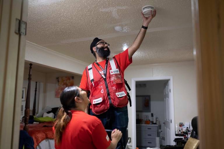 Un voluntario de la Cruz Roja ayuda a otro a instalar detectores de humo