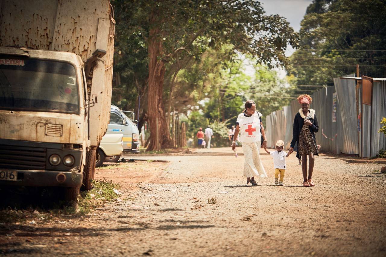 September 27, 2018. Nairobi, Kenya. Prince (middle) walks alongside his mother, Lydia Odinga, and Red Cross volunteer, Felista Njenga, to the local health center to receive vaccinations.  The Red Cross has educated me and my neighbors about the importance of our children receiving vaccinations. My son was 4 months late receiving one of his measles doses, so I was afraid of taking him to the health center but the volunteer convinced me to go,  says Lydia Odinga, from her home in Nairobi, Kenya. Lydia received a visit from Red Cross volunteer, Felista Njenga, who helps ensure kids in the dense urban community receive lifesaving vaccines such as those for measles and rubella.  I volunteer because, as a mother, my desire is to have a healthier community free of diseases,  says Felista. Local Red Cross volunteers go door-to-door to identify children who are missing routine immunizations, update vaccination records at local health centers, encourage parents and caregivers to have their children vaccinated, and follow up with families to confirm receipt of the recommended vaccinations. Each year in Kenya, more than 350,000 children miss their scheduled routine vaccinations leaving them vulnerable to vaccine-preventable diseases such as measles and rubella. The American Red Cross and the Kenya Red Cross have been working together to strengthen community-level routine immunization systems in both rural and urban counties.   Measles is one of the most contagious and severe childhood diseases. Every day, it takes the lives of hundreds of children around the world. Even if a child survives, measles can cause permanent disabilities, such as blindness or brain damage. But there is hope. Since 2001, the American Red Cross and our partners in the Measles & Rubella Initiative have vaccinated more than 2 billion children around the globe. The Red Cross plays a pivotal role in vaccination campaigns worldwide: local volunteers use mass media, rallies, door-to-door visits and educat