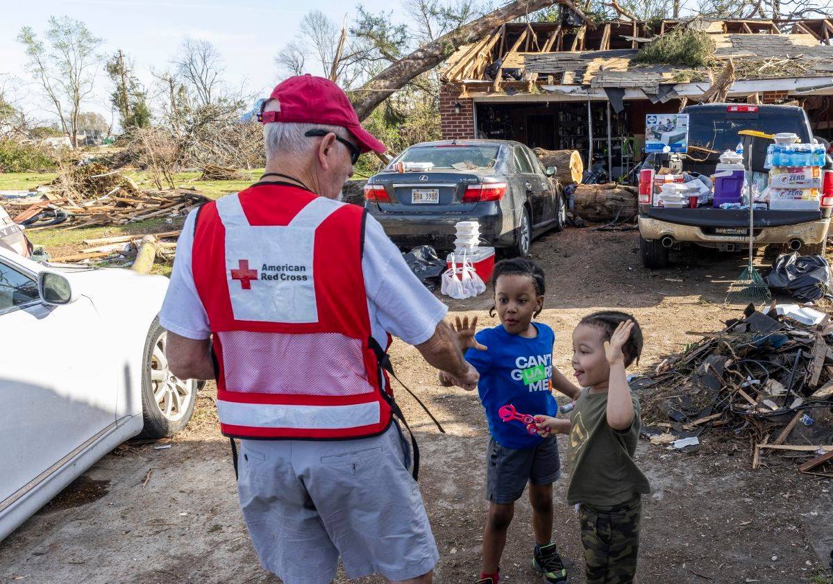 March 27, 2023. Rolling Fork, Mississippi. 
Red Cross volunteer Terry Smith visits with Justin Russell and Jonah Russell. As many as 2,000 structures across Mississippi received major damage or were destroyed by tornadoes on Friday. Smith, who deployed in from Tampa Bay, Fla., was part of a team serving warm meals in one of the hardest-hit communities. 
Photo by Scott Dalton/American Red Cross