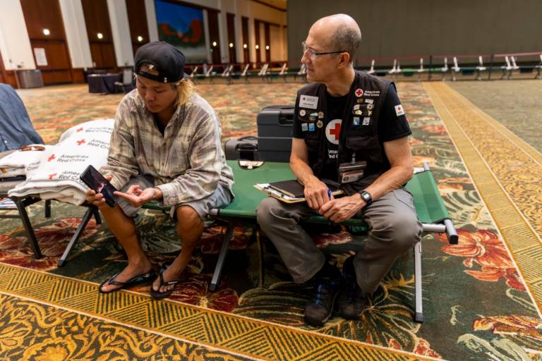 Chris Phillips shows American Red Cross shelter worker Richard Byam pictures he took as he fled the deadly flames that swept through Lahaina