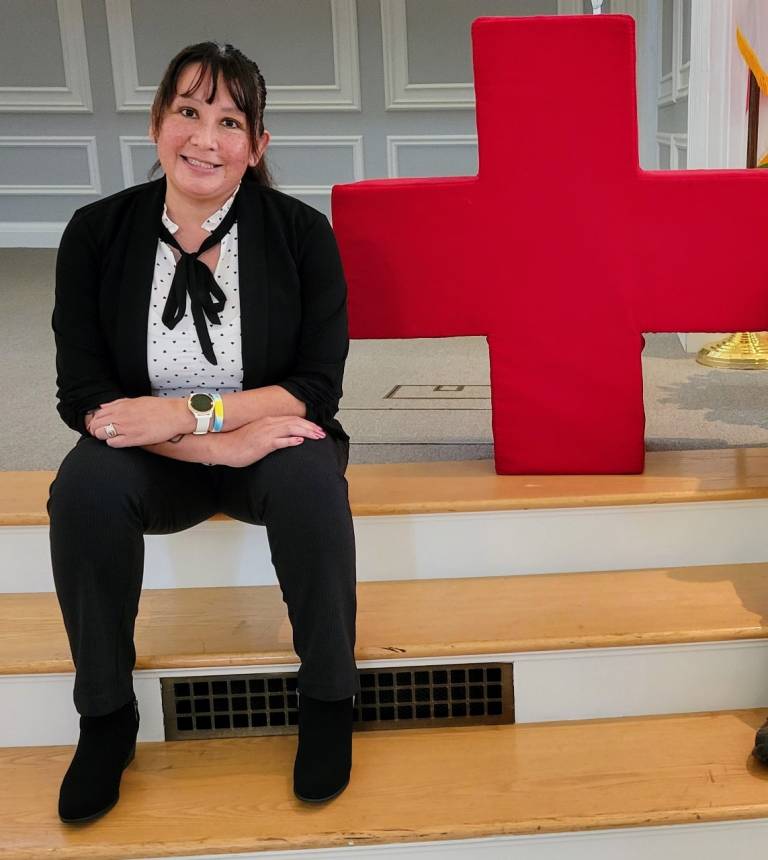 Alexis War seated on a bench in front of a Red Cross flag