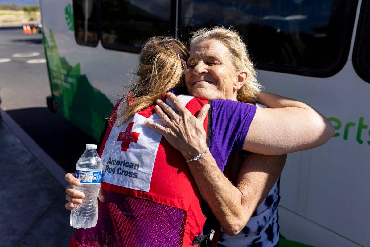August 18, 2023. Kihei, HawaiiAmerican Red Cross volunteer Caitlin Harrowby embraces Teresa Randolph-Sherlock before she boards a shuttle bus in front of the Red Cross congregate shelter at the South Maui Community Park Gymnasium in Kihei. Randolph-Sherlock is moving into a nearby hotel room where she will continue to have access to Red Cross care and support.Photo by Scott Dalton/American Red Cross