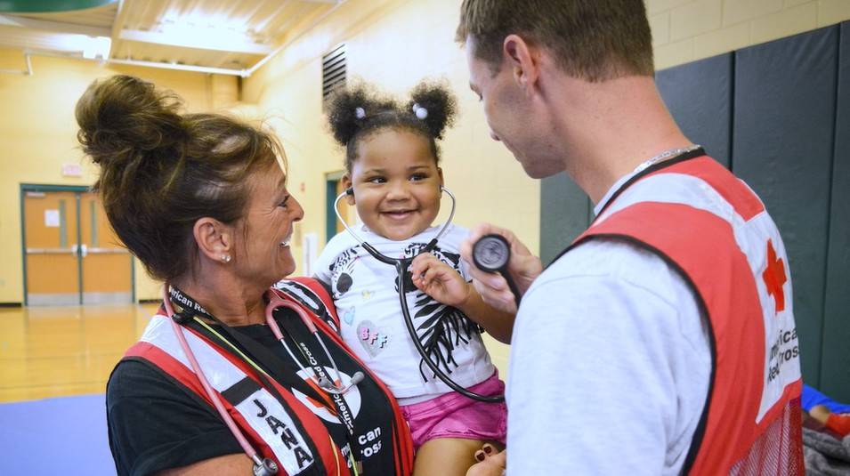 A Red Cross volunteer and a Red Cross nurse check on a young child