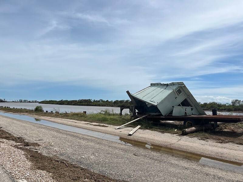 Cobertizos y garajes dañados junto con escombros y madera flotante a lo largo de las orillas de un río inundado