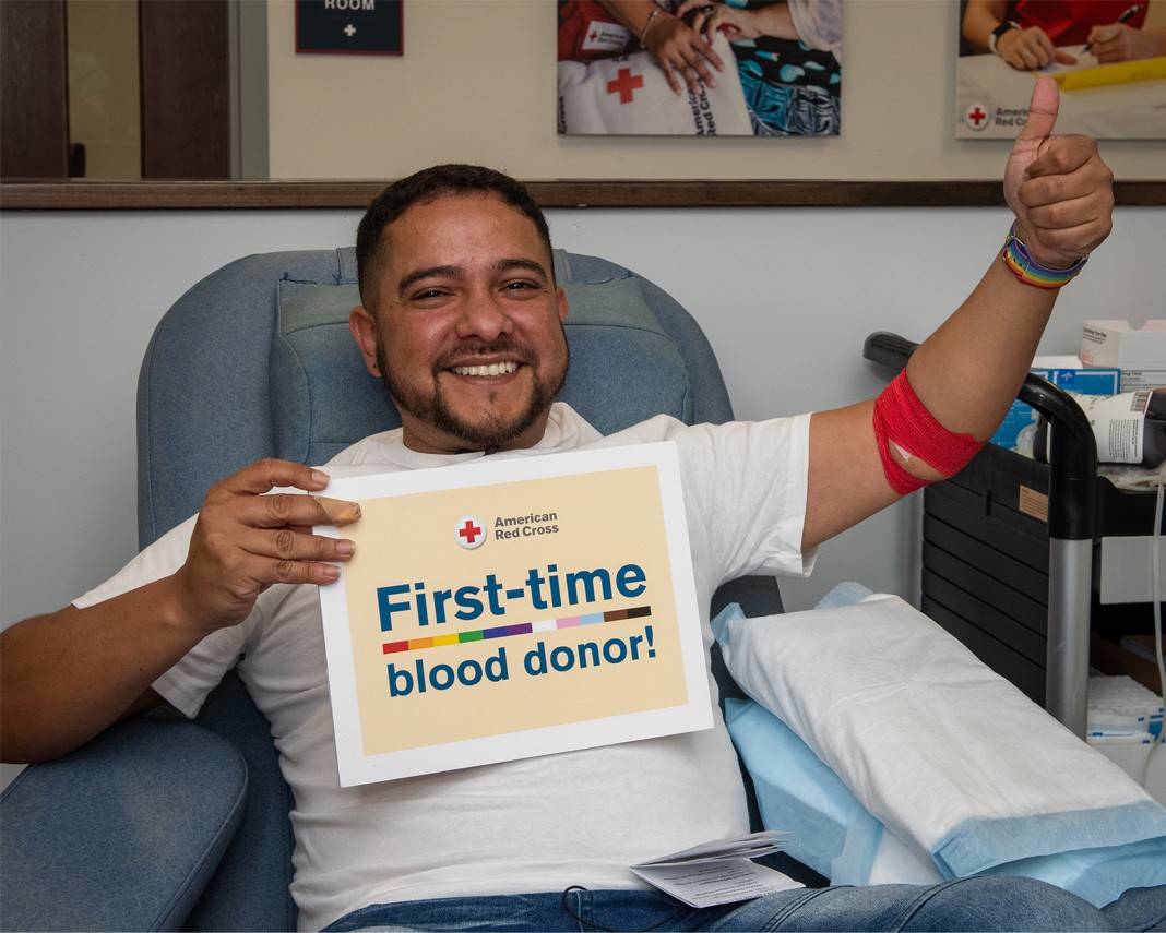 A man at a Red Cross blood donation center is holding a sign that says first time blood donor