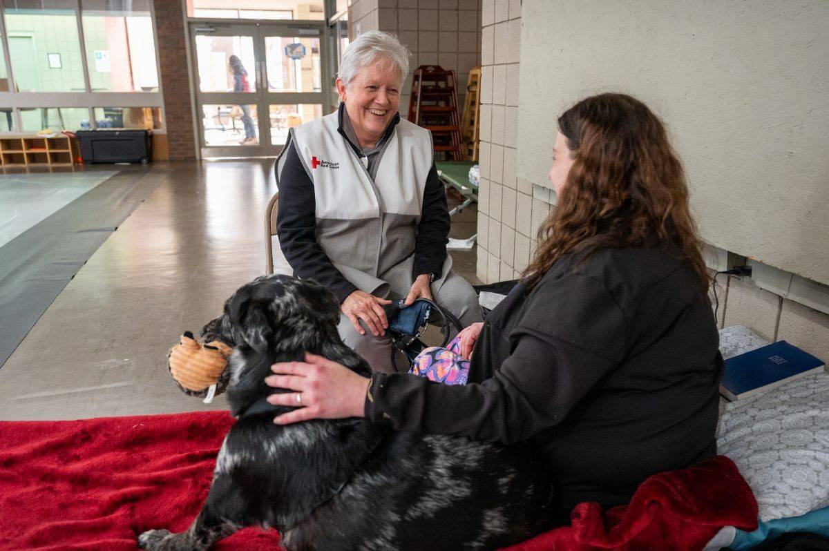 Woman in Red Cross vest takes the blood pressure of another woman in a Red Cross disaster shelter.