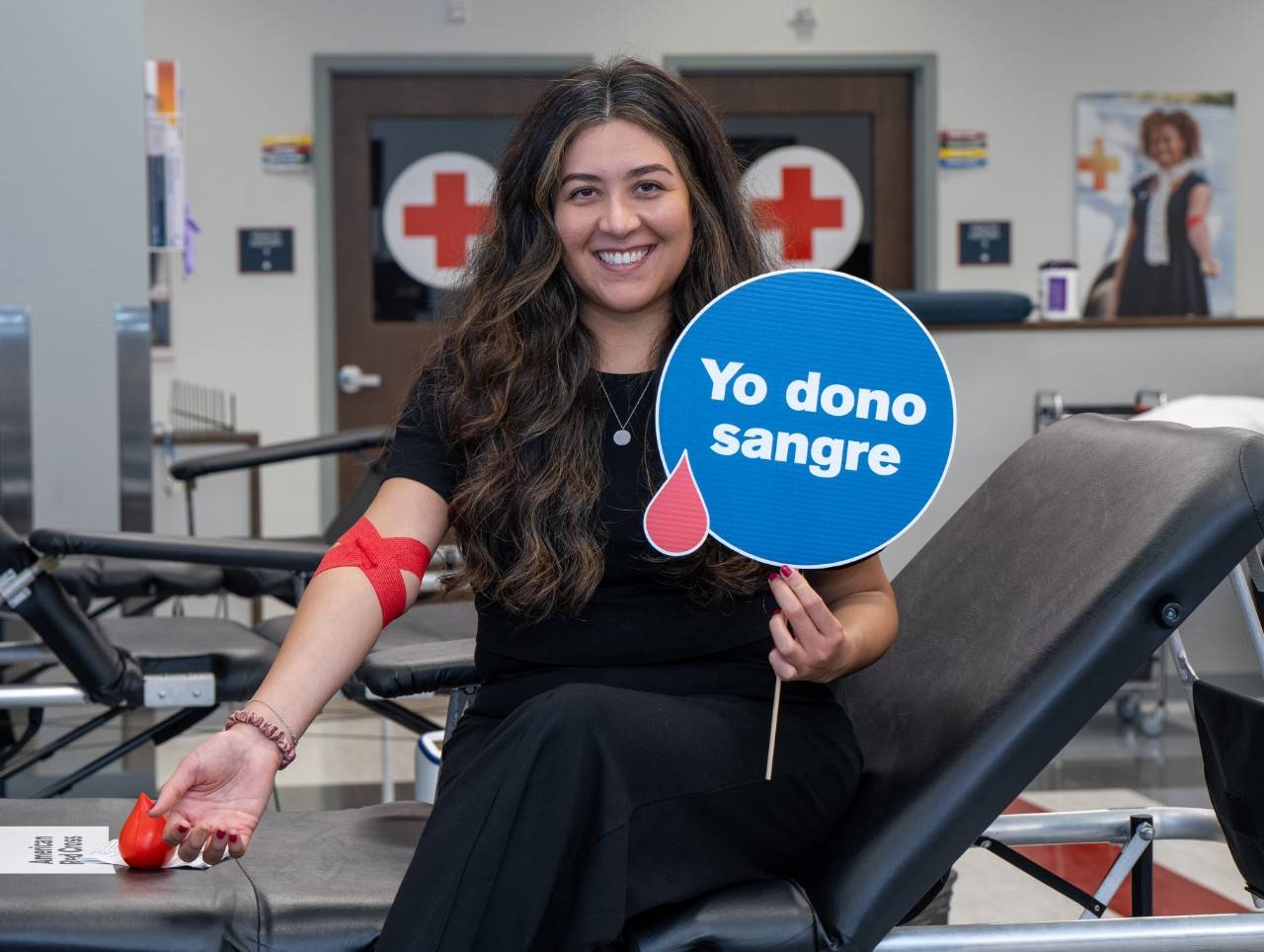 Woman sits on blood donor bed holding up sign