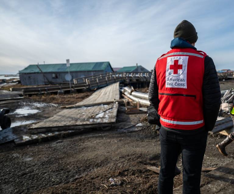 man in Red Cross vest studies damage in Alaskan village