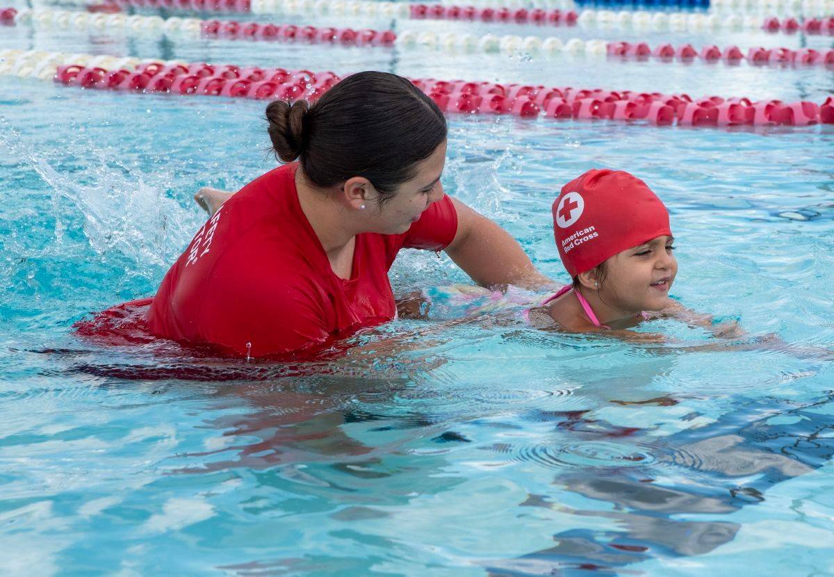 Photo illustrates an instructor teaching a young girl how to swim.