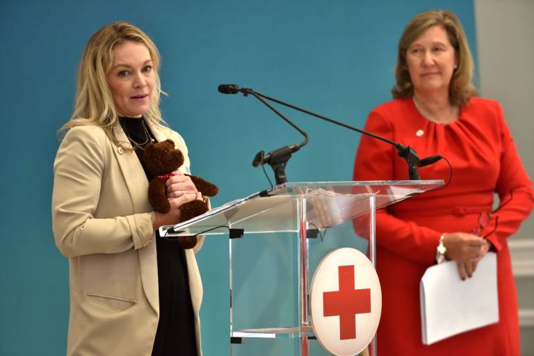 woman stands at podium holding a stuffed bear