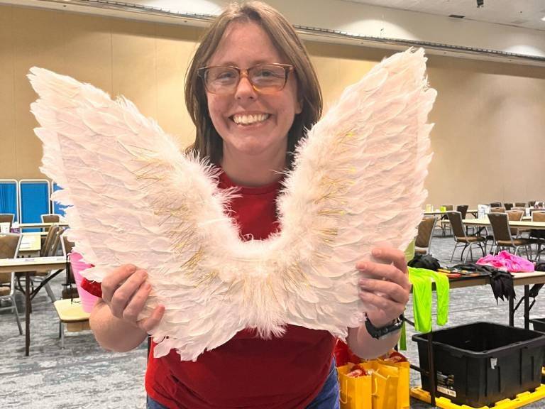 Woman in Red Cross vest holds up angel wings.