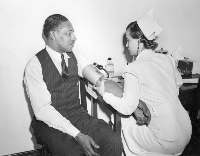 In older photo, man has his blood pressure taken.