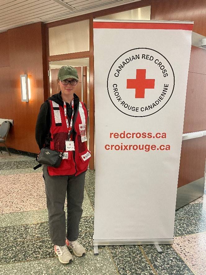 Woman in Red Cross vest stands next to a Canadian Red Cross sign.