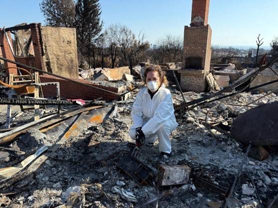 Woman in white hazmat suit in the wreckage of her burned home.