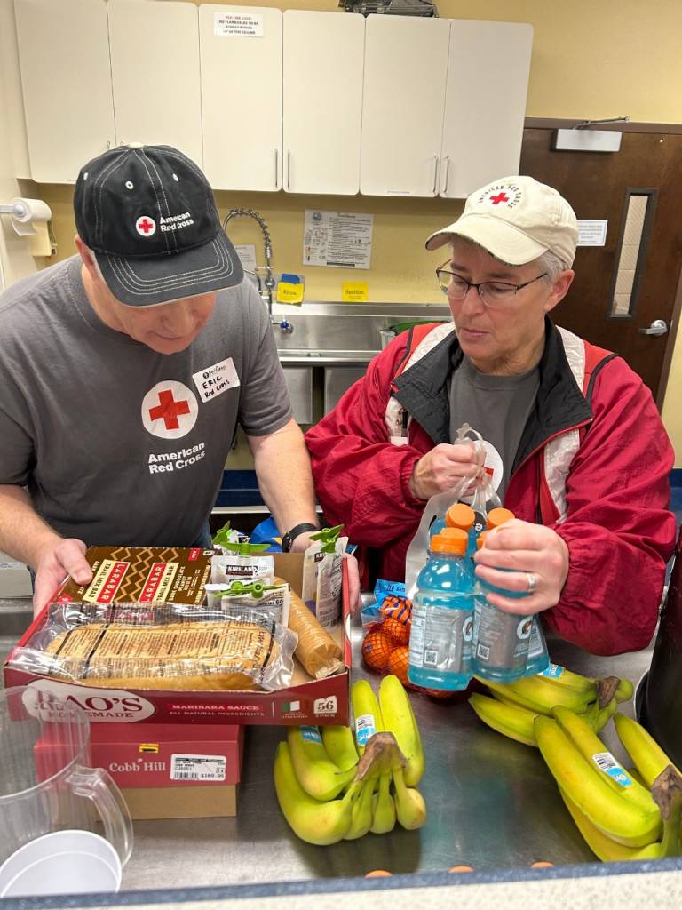 A man and woman in Red Cross vests prepare to serve a meal at a shelter
