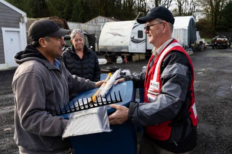 man in Red Cross vest hands another man cleaning supplies