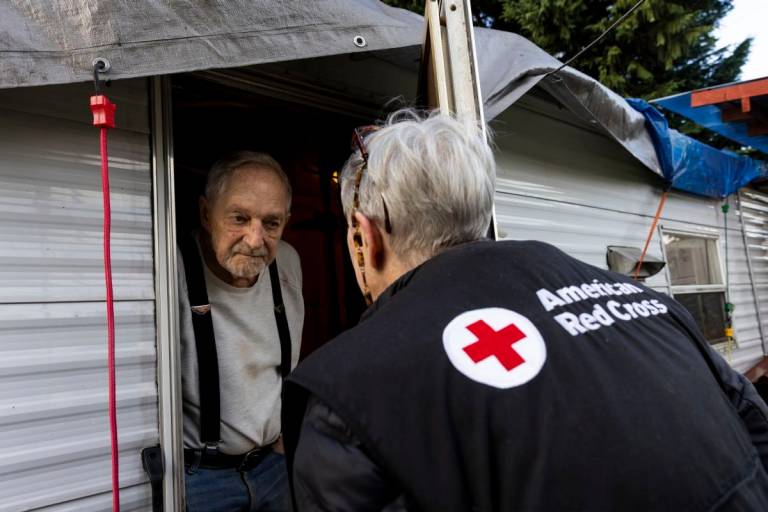 woman in Red Cross clothing speaks to another woman through the door of her home