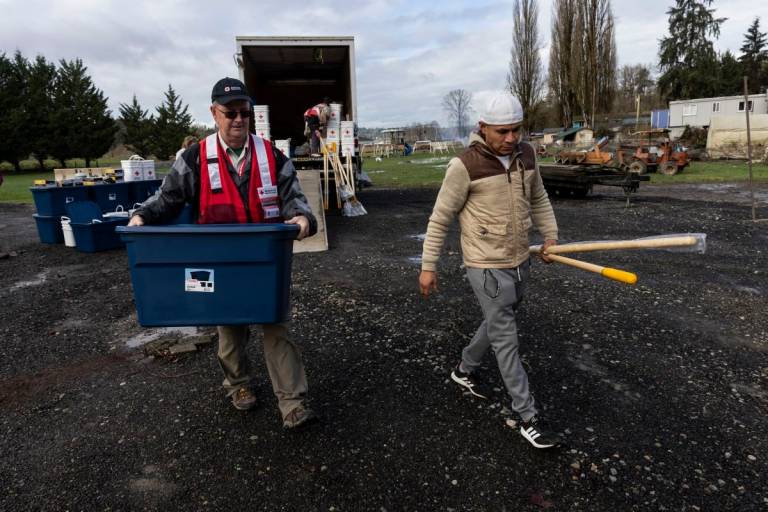 Red Crosser carries cleaning supplies for flooding victim