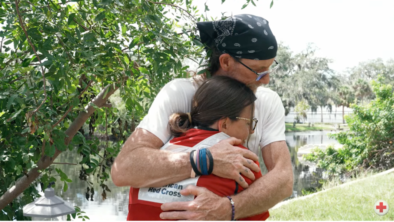 Two people embrace, one in Red Cross vest