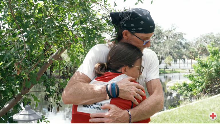 Two people embrace, one in Red Cross vest