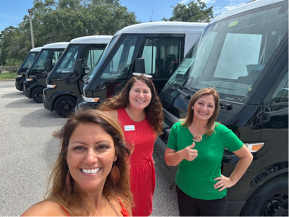 Three women stand in front of donated vans.