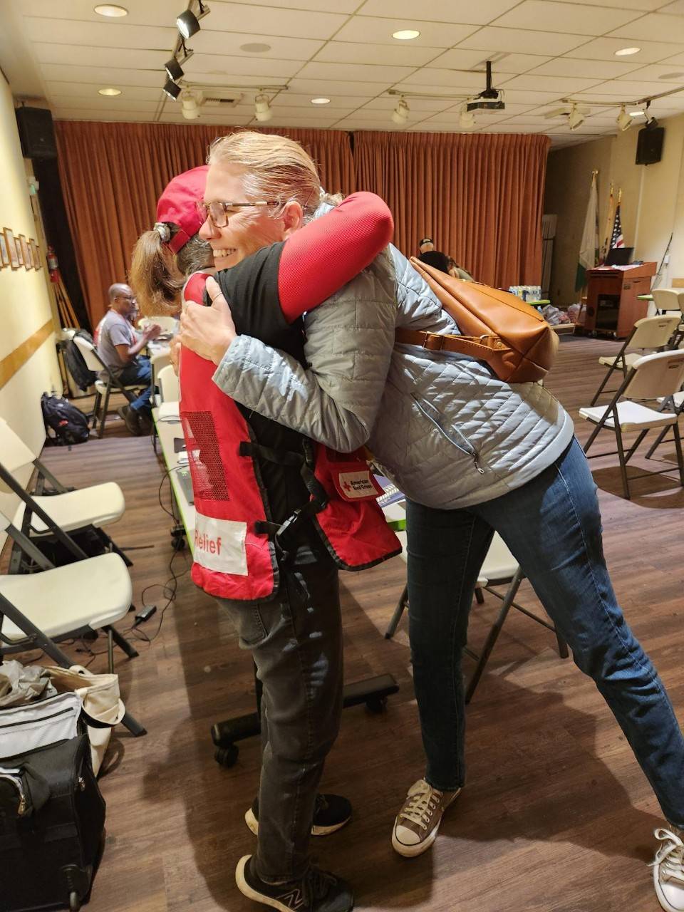 A woman embraces another woman wearing a Red Cross vest after receiving financial assistance.