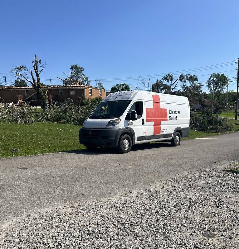 Red Cross emergency vehicle passing through neighborhood with damage from tornado