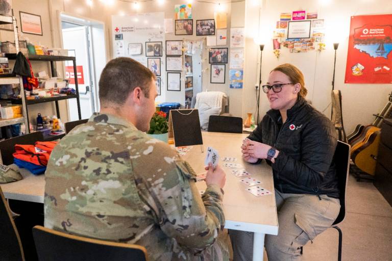 A Red Cross expeditionary staffer and a service member relax together and play cards on a forward operating site in Poland.