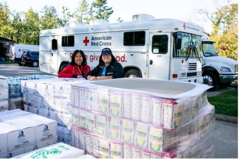 Photo of Mariana Vimbela and Erica Frausto Aguado standing in front of disaster relief supplies.