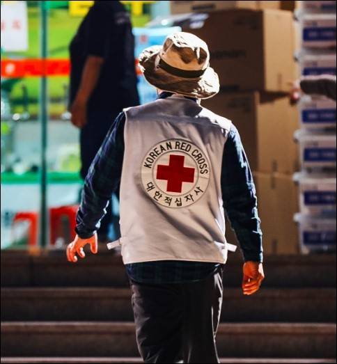Man in Red Cross vest seen from the back