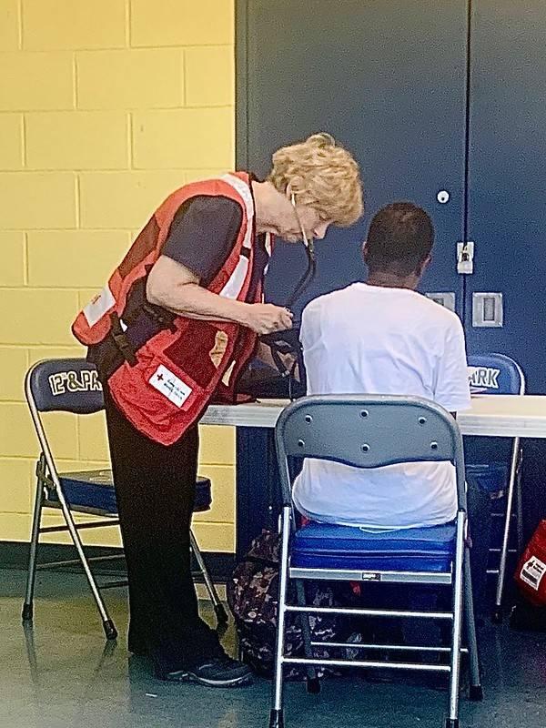 nurse in Red Cross vest checks on a man in a shelter