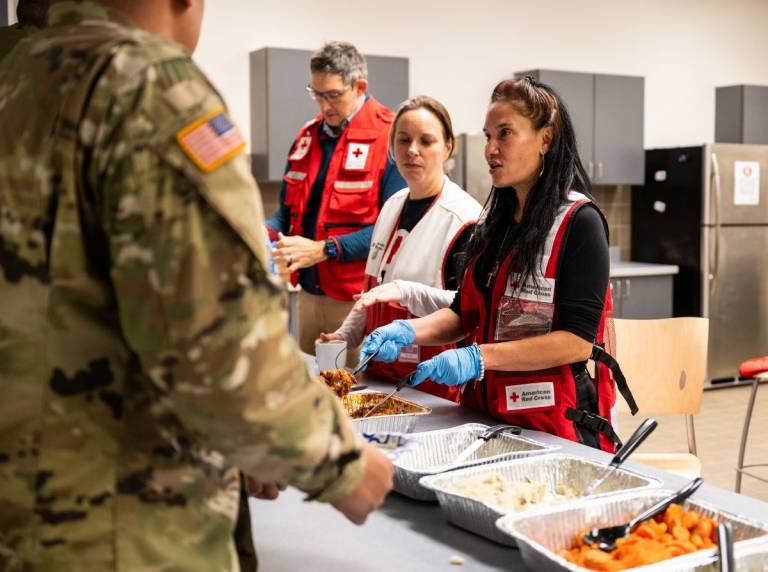 women in Red Cross vests serve meals to men in uniform